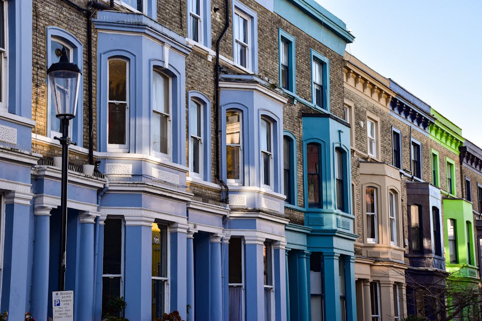 A row of three-story residential buildings in Notting Hill featuring distinct color schemes, with the first building painted in beige, the second in dark blue, the third in vibrant lime green, and the