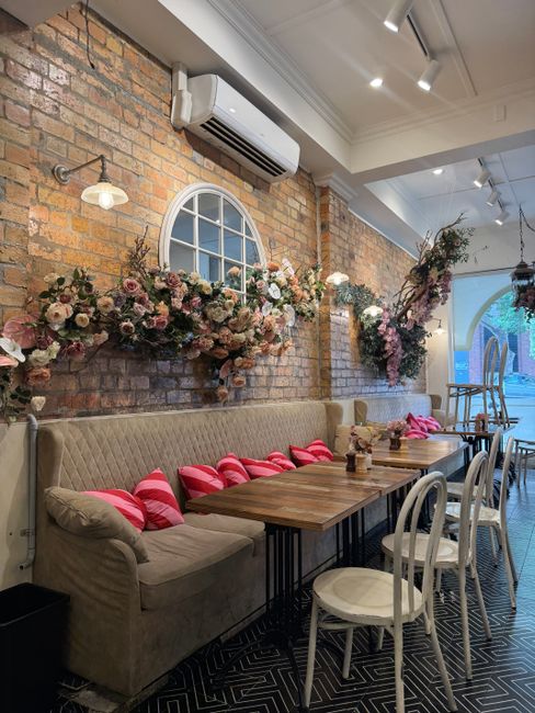A cozy dining area in Westbourne Grove cafes featuring a light wooden table with a smooth surface and a natural finish. The table is set with a single glass bottle of water, a small glass vase with ye