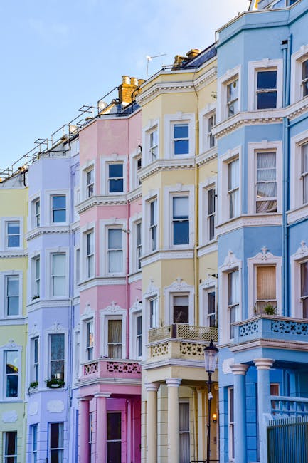 A row of multi-story residential buildings painted in pastel shades of yellow, pink, blue, and white, featuring ornate architectural details such as decorative molding and cornices. The buildings have